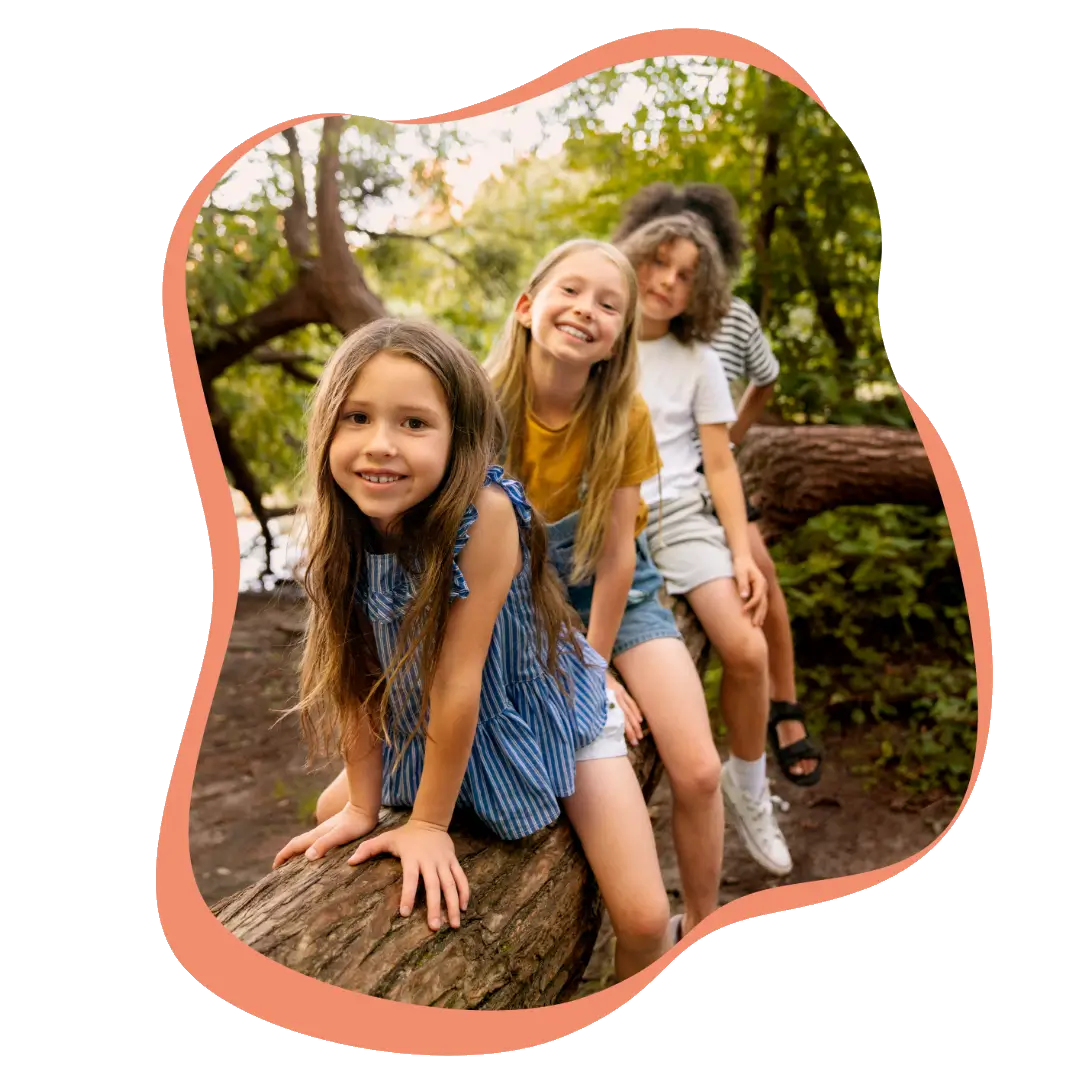 Mehrere Kinder sitzen im Wald auf einen Baumstamm.